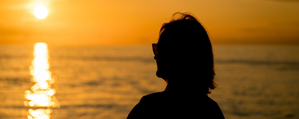 silhouette of woman looking at sunset over water